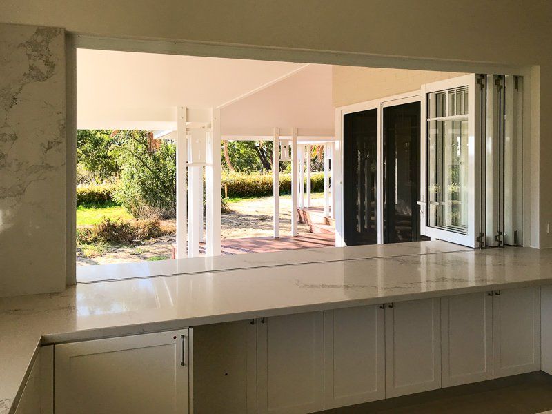Interior view of a kitchen counter with a pass-through window to a porch. White cabinets and marble counters.