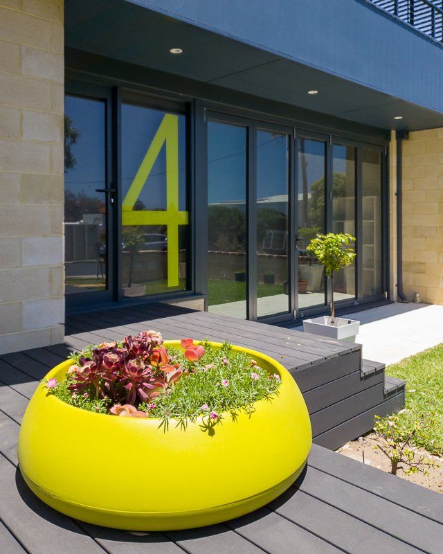 Yellow planter with greenery on a gray deck, modern building with a large 