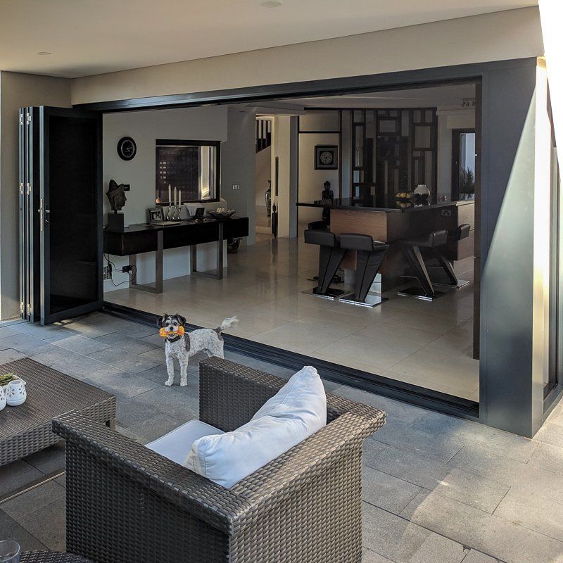 Patio doors open to a living space; a small dog stands with a toy; patio furniture.