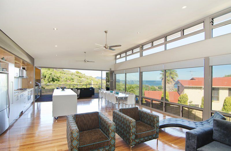 Open-concept living space with ocean views. Brown armchairs, a white kitchen island, and large windows are present.