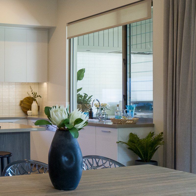 Dining table with vase of flowers, kitchen in background. Window with exterior view.