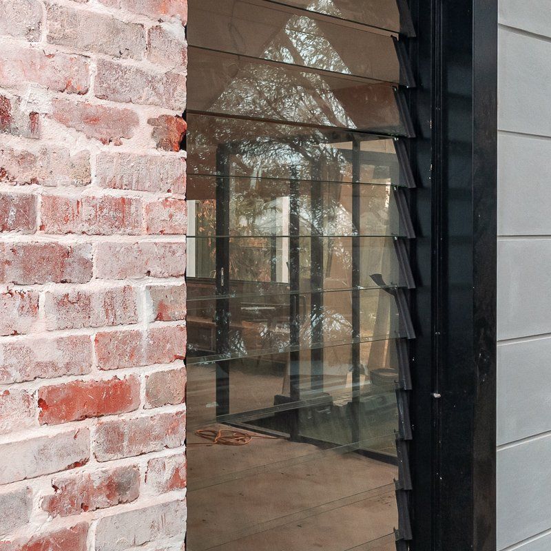 Exterior view of a building with brick wall and louvered glass window reflecting the surrounding environment.