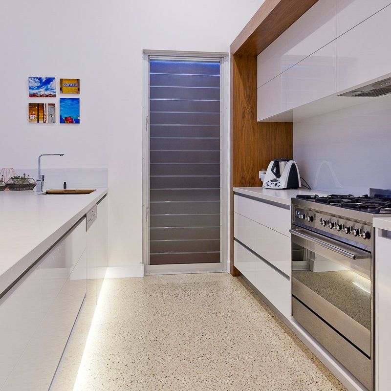 Modern white kitchen with stainless steel oven, white countertops, and terrazzo floors.