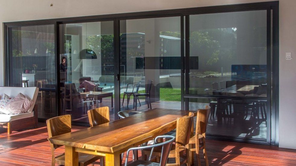 A patio with a wooden table, chairs, and large glass sliding doors looking into a home.