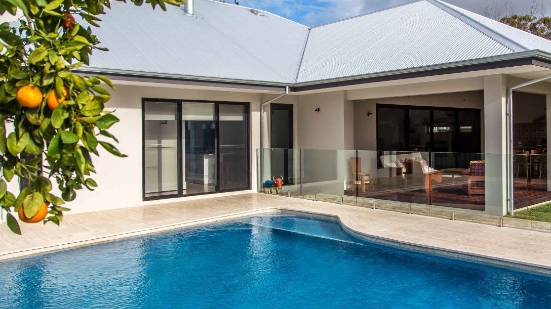 Backyard with a swimming pool, citrus tree, and modern house with a covered patio.
