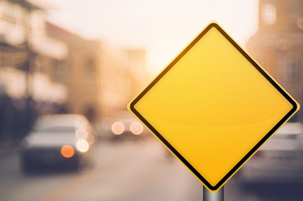 Yellow diamond-shaped warning sign on a blurry street background.