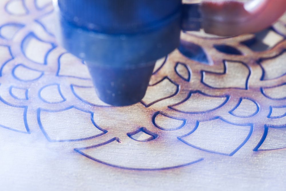 Laser cutter etching a floral design into wood. Blue laser light, close-up.