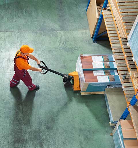 A man is pushing a pallet truck in a warehouse.