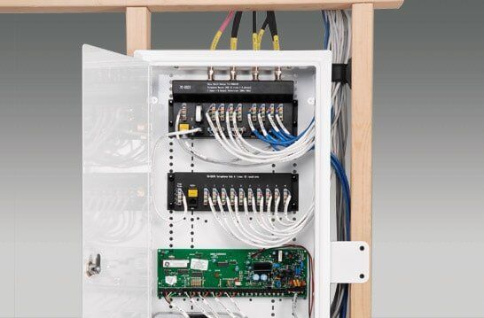 A white network enclosure with wires and electronic components installed within a wooden frame. 