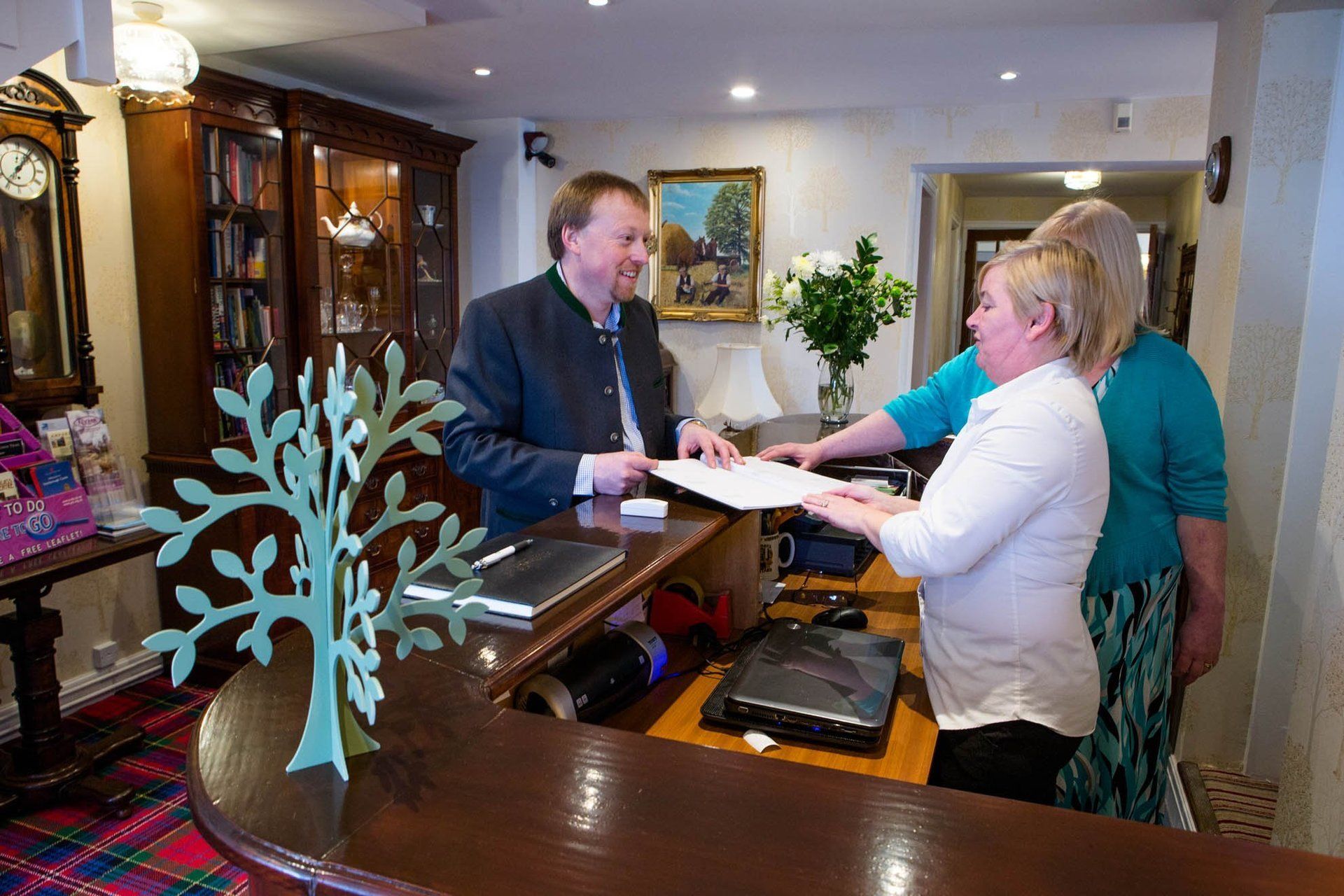 A man is talking to two women at a hotel reception desk.