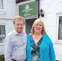 A man and woman are posing for a picture in front of a sign that says deciduous lodge