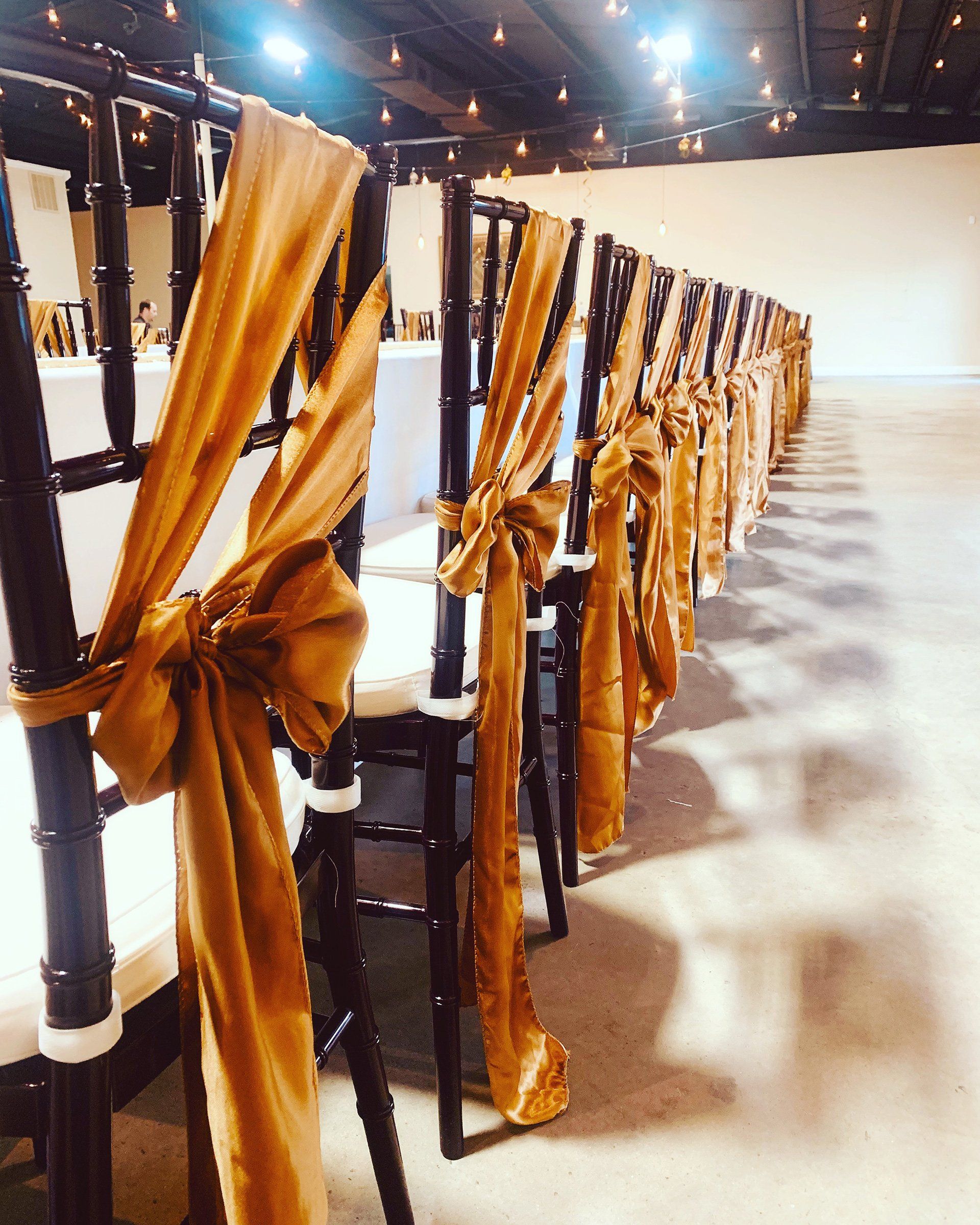 chairs with gold bows on back  lined up along long table with