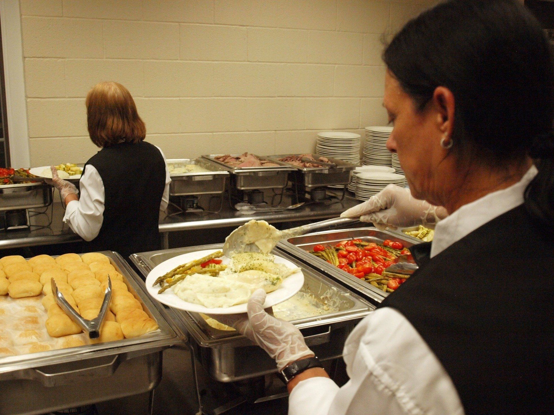 caterers putting food on a plates from buffet