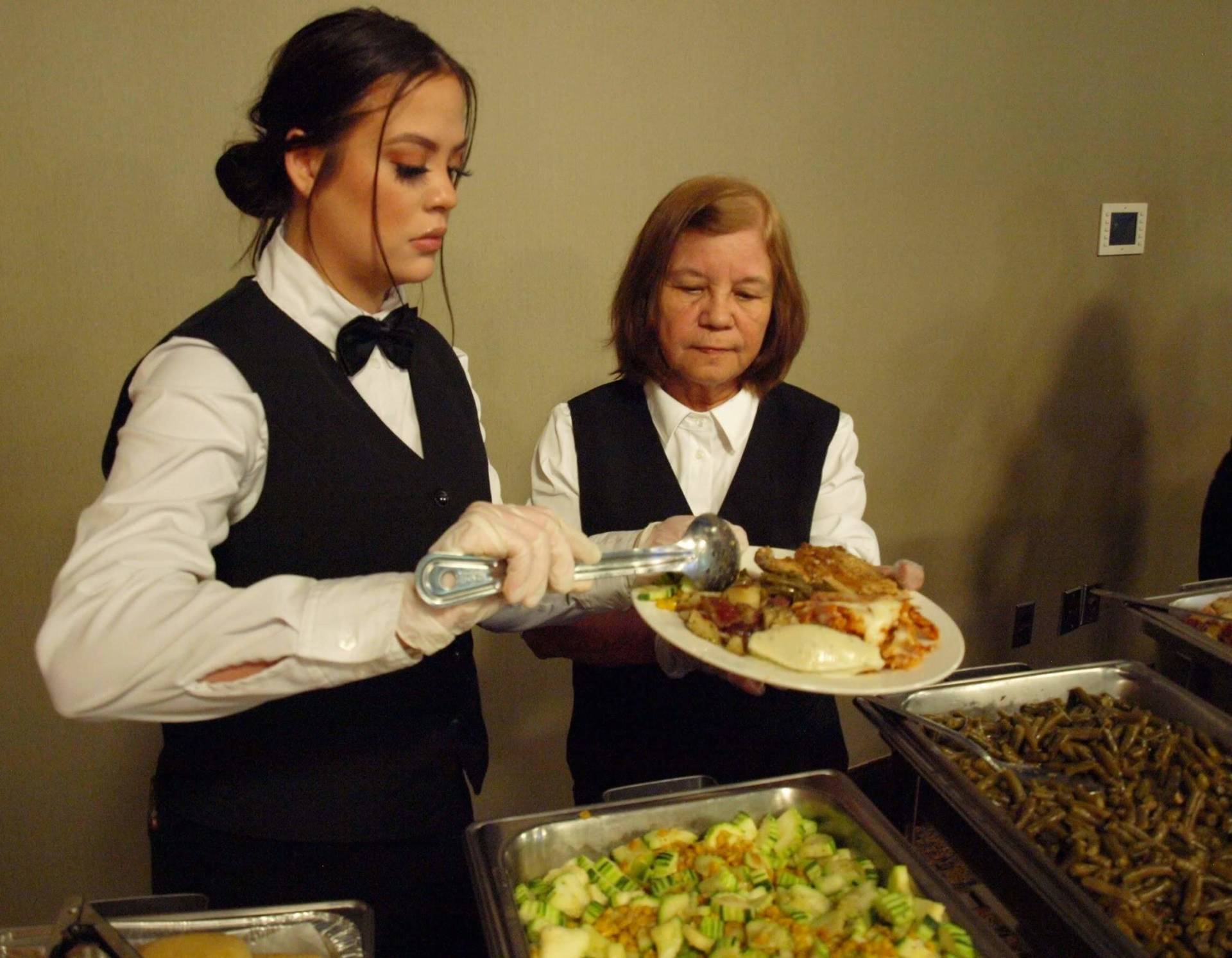 2 female caterer putting food on a plate