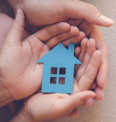 Adult and child hands holding paper house, family home and real estate concept