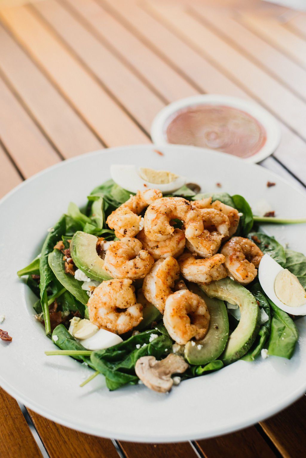 A salad with shrimp , avocado , spinach , mushrooms and eggs on a wooden table.