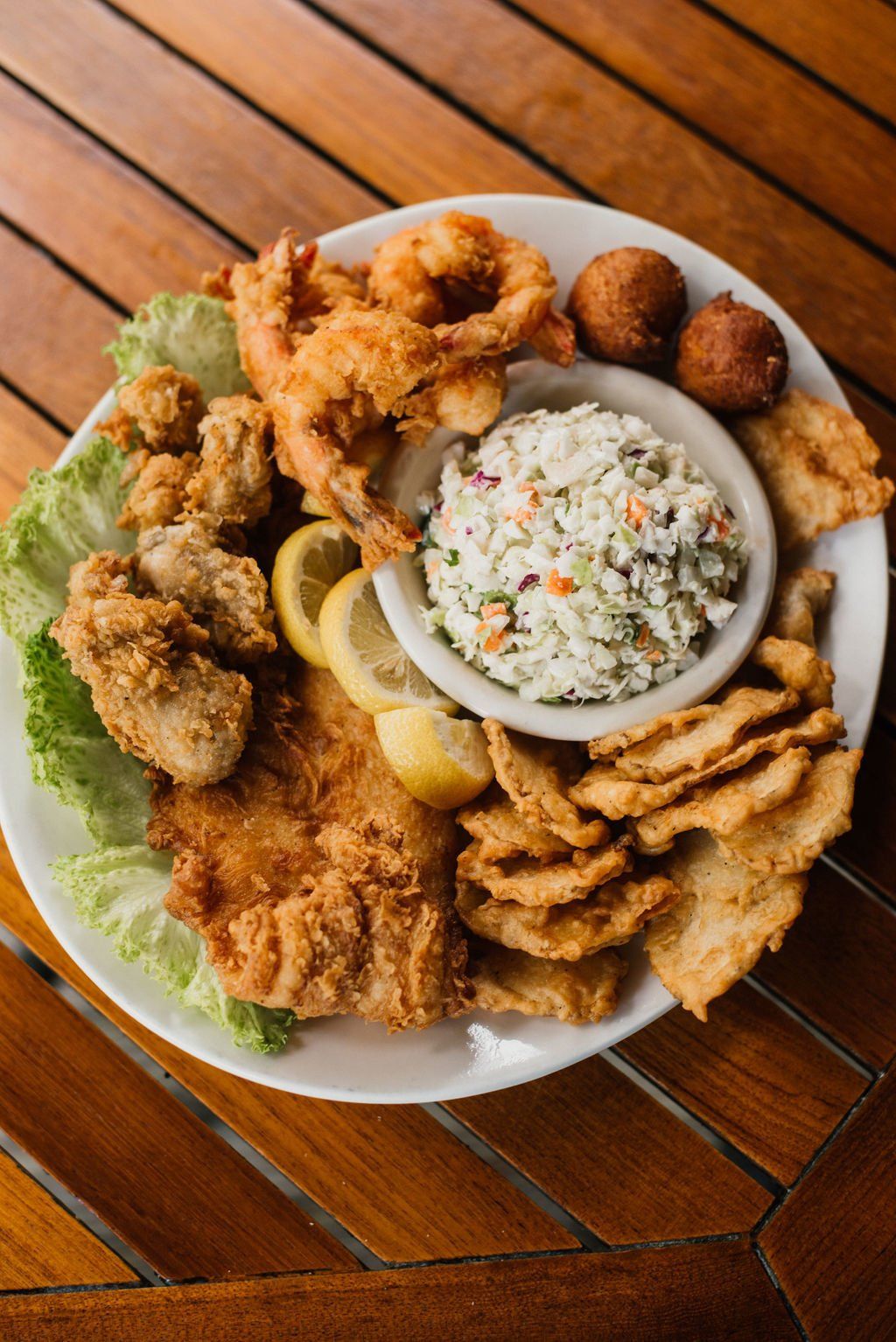 A white plate topped with fried food and coleslaw on a wooden table.
