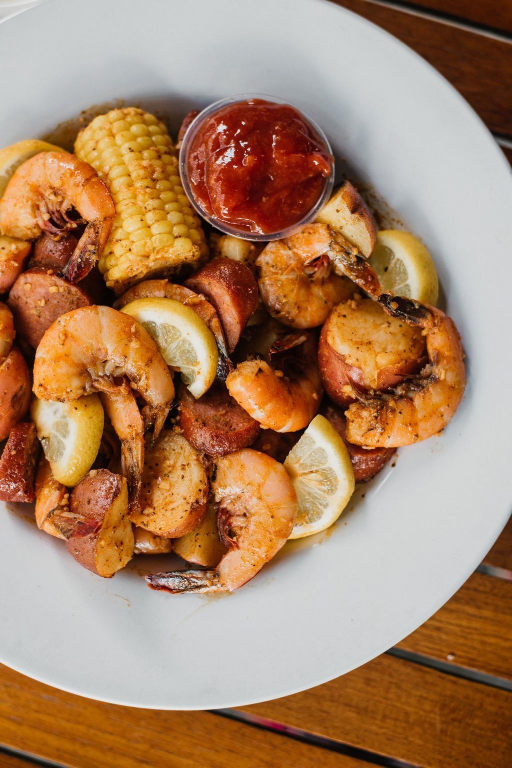 A white plate topped with shrimp , corn on the cob , potatoes and sausage.