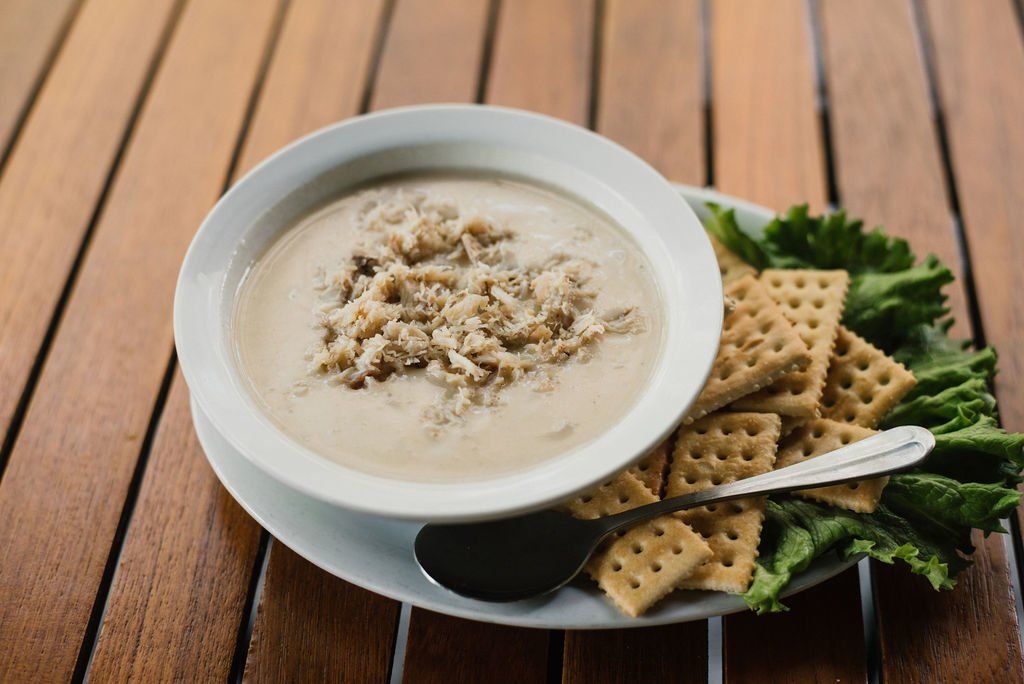A bowl of soup and crackers on a plate on a wooden table.