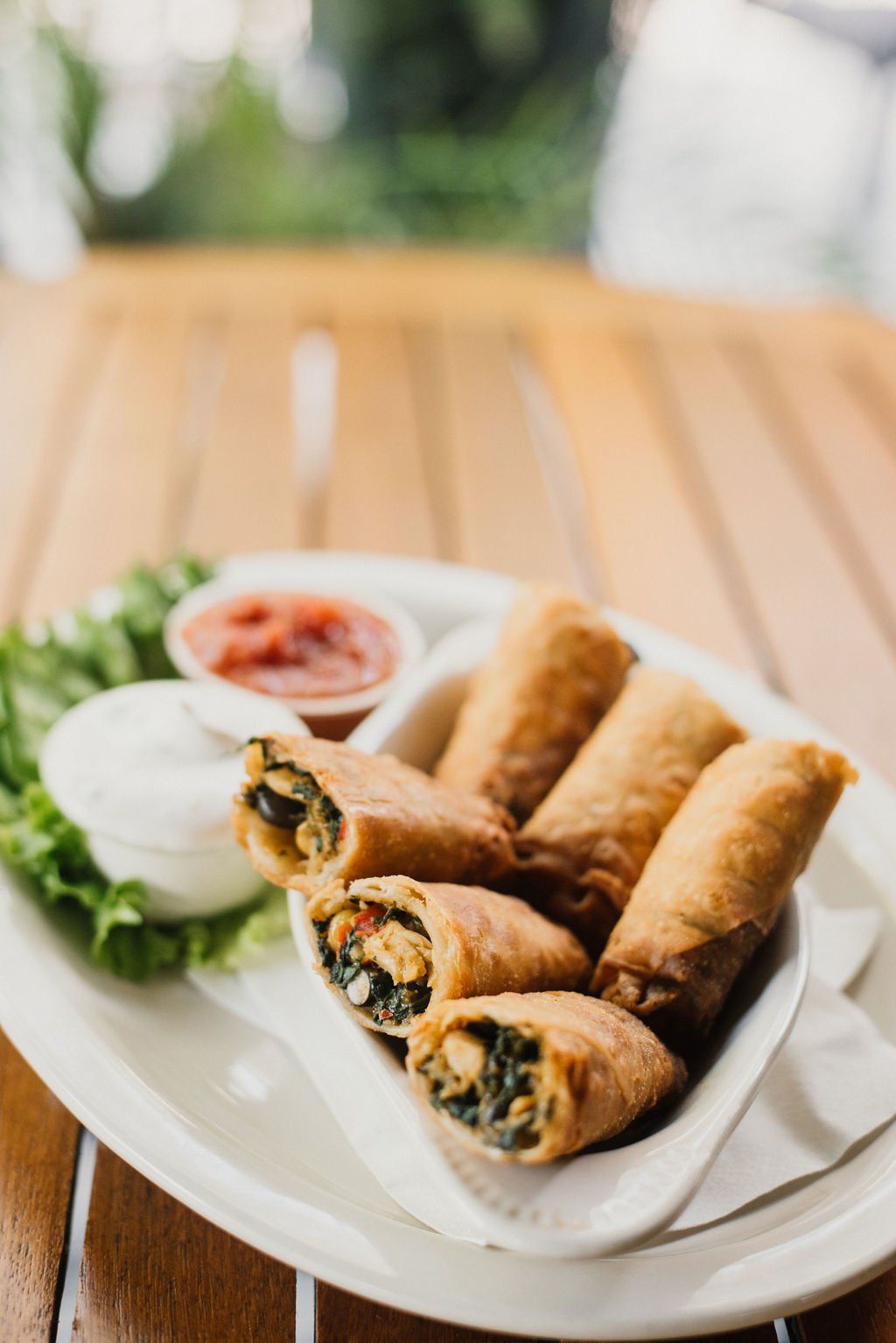 A white plate topped with spring rolls and sauces on a wooden table.