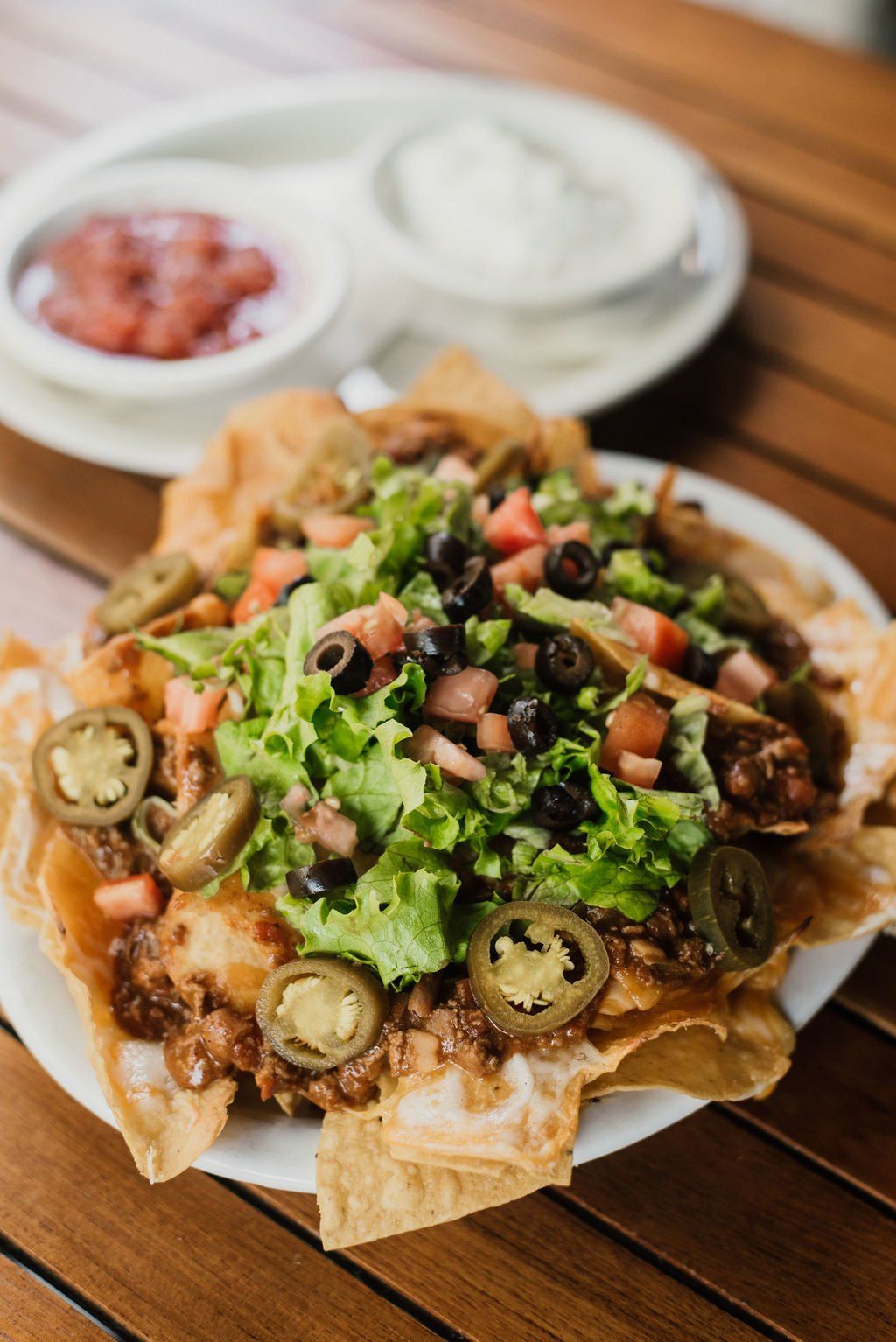 A close up of a plate of nachos on a wooden table.
