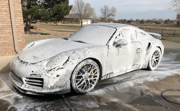 a porsche is covered in foam in a driveway .