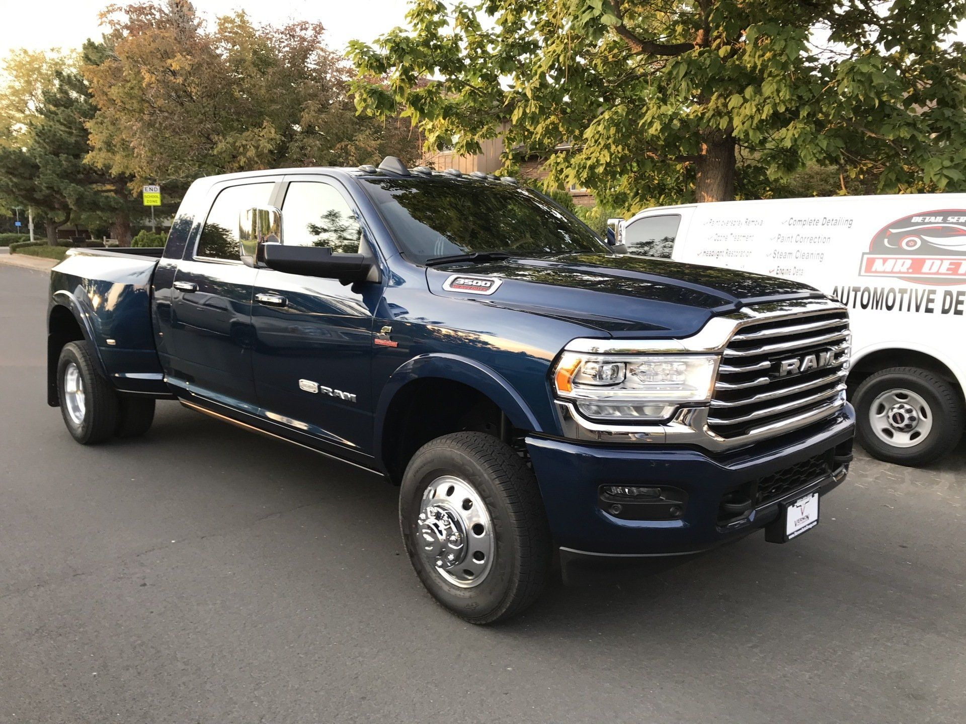 a blue ram truck is parked on the side of the road next to a white van .