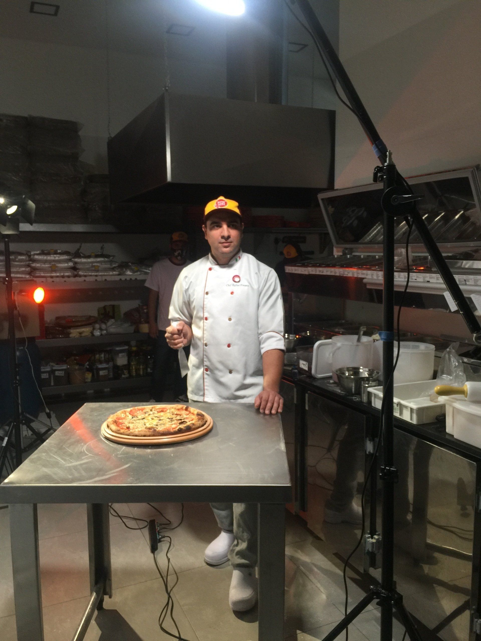 Um chef está ao lado de uma pizza sobre uma mesa