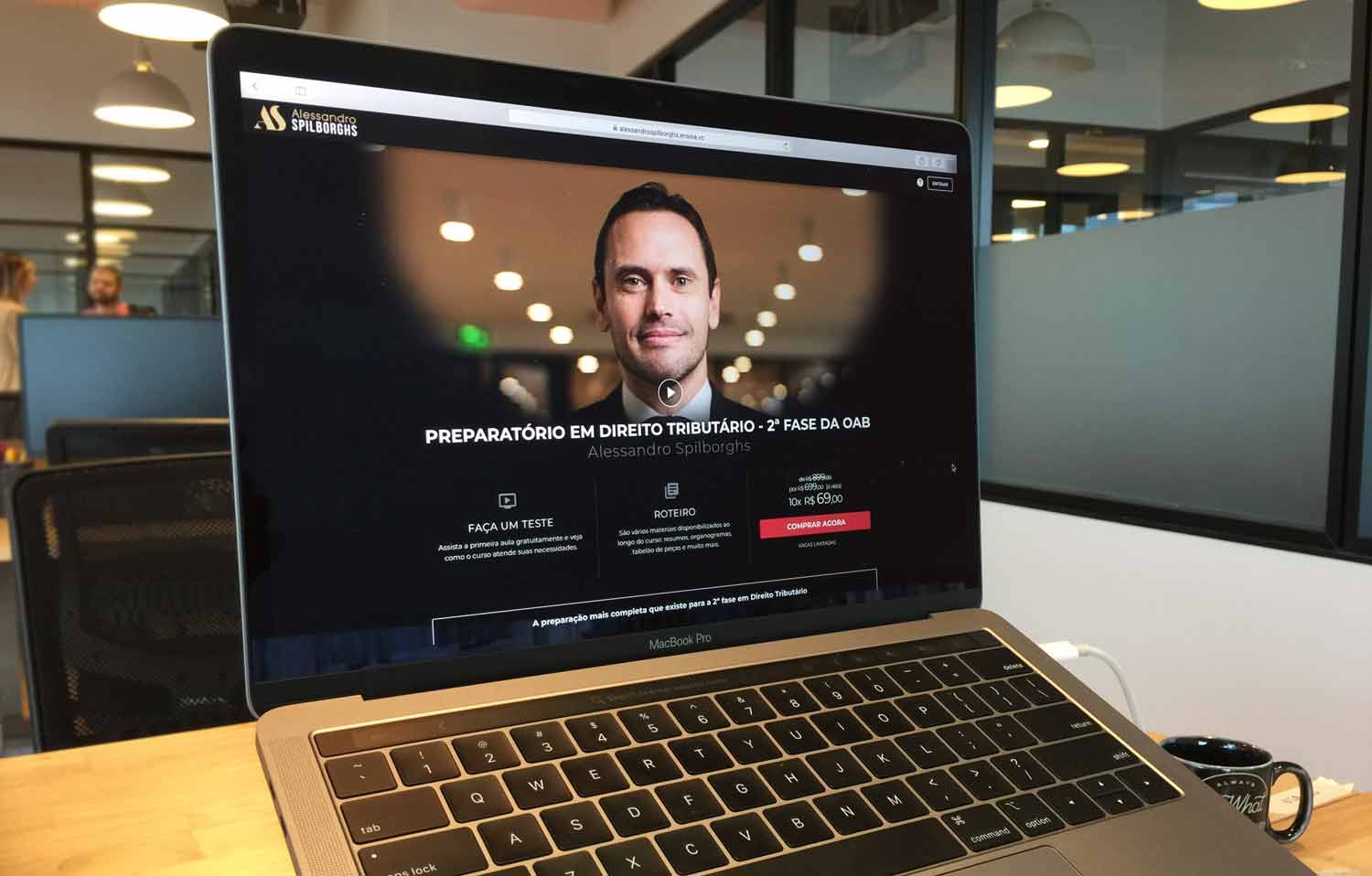 Um laptop está aberto diante de uma tela com o rosto de um homem.
