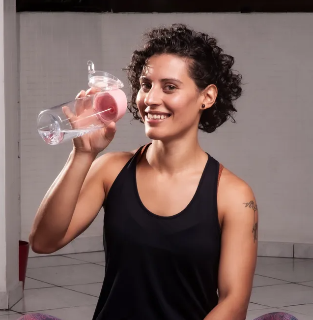 Uma mulher com uma blusa preta está bebendo de uma garrafa rosa