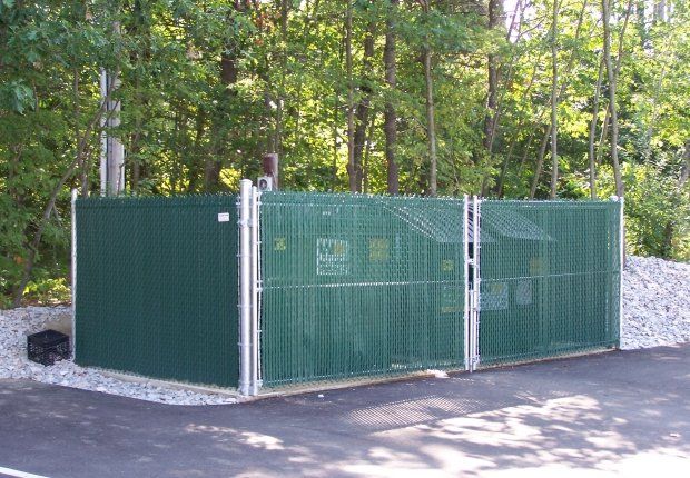 a green fence with a gate is surrounded by trees .