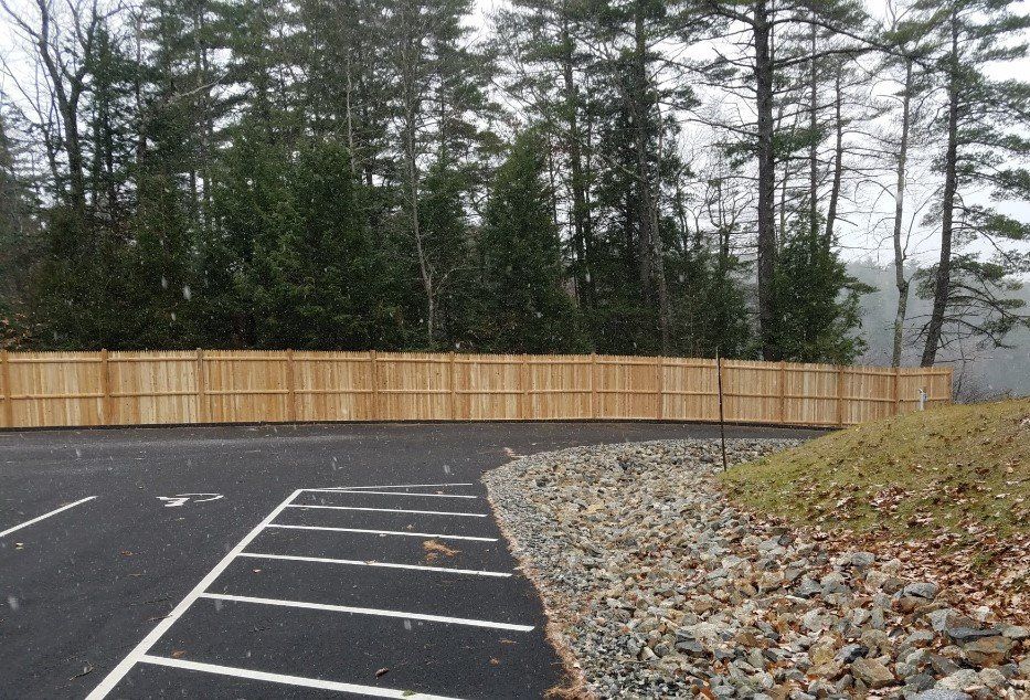 a wooden fence surrounds a parking lot with trees in the background .