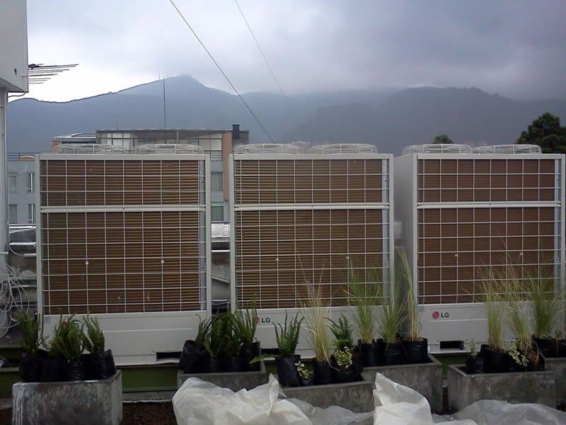 Una fila de acondicionadores de aire con plantas delante de ellos.
