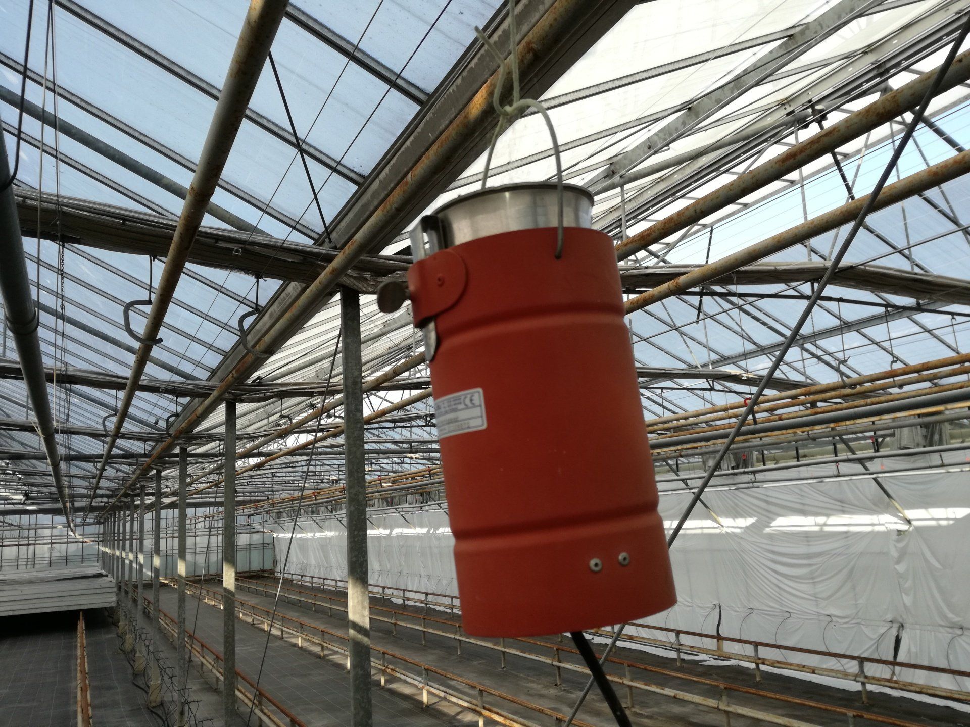 Oranje cilindervormige verwarming, opgehangen aan het plafond van de kas.
