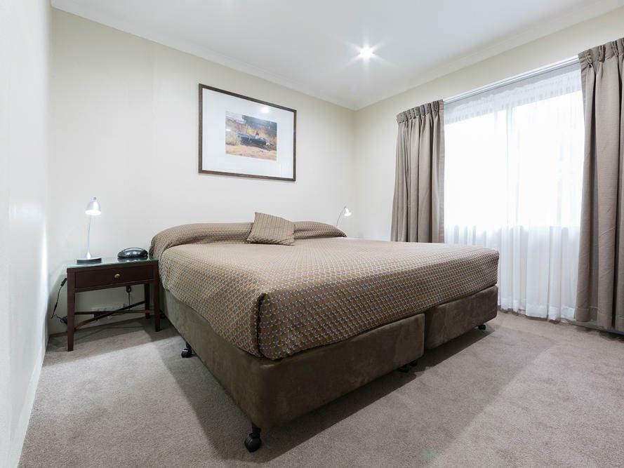 Bright bedroom with a brown bed, beige carpet, nightstand, framed art, and window curtains
