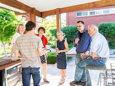 Group of people chatting on a porch around a stone outdoor bar, with drinks and a brick building in the background
