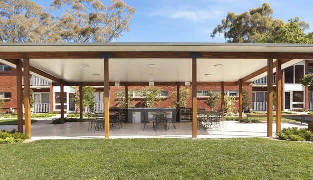 Open-air courtyard with shaded seating, brick buildings, and green lawn under a clear sky