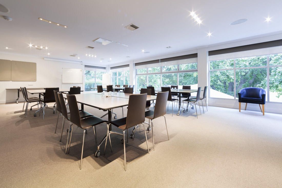 Bright conference room with tables, chairs, and large windows overlooking greenery