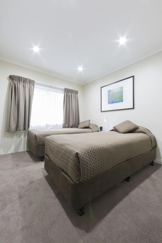Small bedroom with two single beds, beige bedding, gray curtains, and ceiling lights