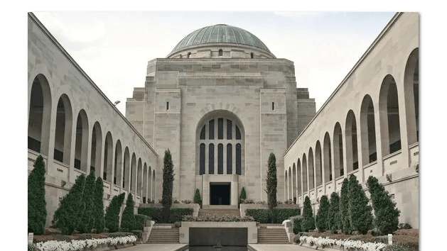 Stone memorial courtyard with arched colonnades and a domed building at the far end