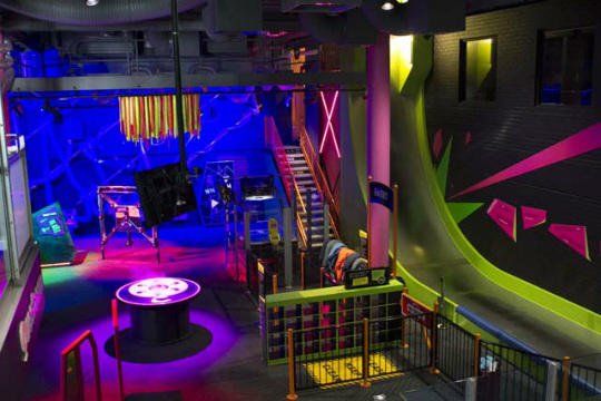 Neon-lit indoor venue with blue and pink lights, round platform, stairs, and railings.