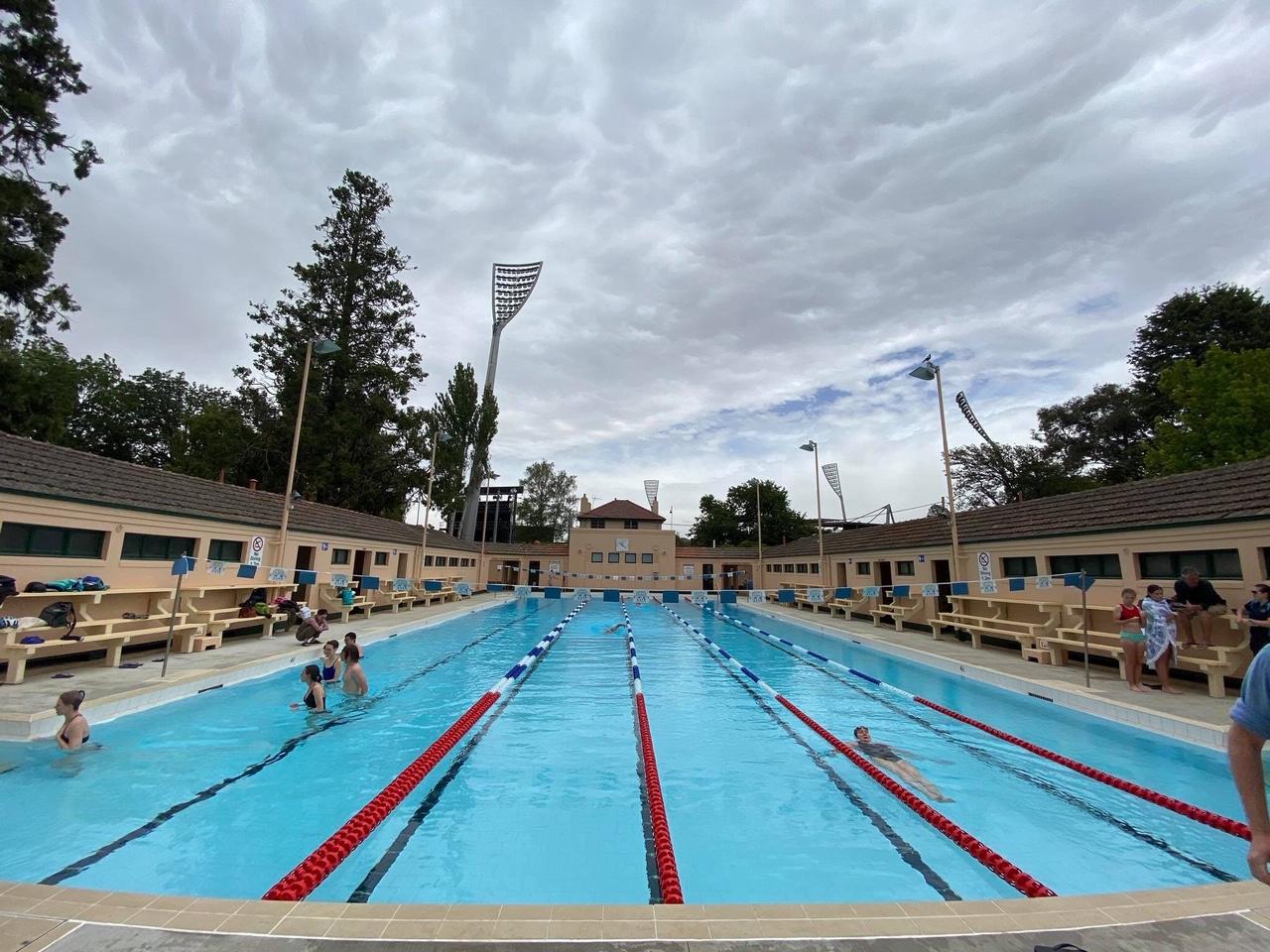 Outdoor lap pool with swimmers under a cloudy sky, seen from the end of the lanes.
