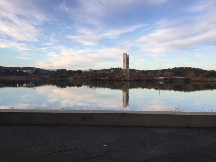 Tall tower reflected in a calm lake at sunset under a blue, cloud-streaked sky
