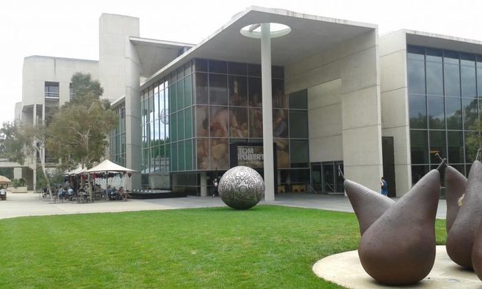 Modern glass-fronted building with green lawn and abstract metal sculpture in front