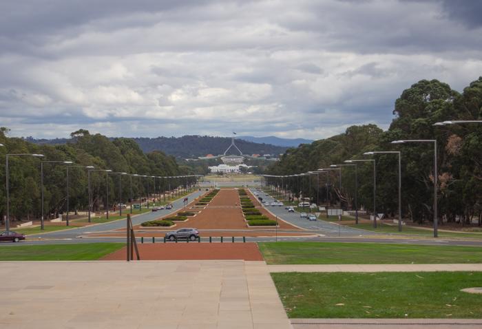 Wide avenue leading to a distant memorial, lined with trees and grassy medians under a cloudy sky.