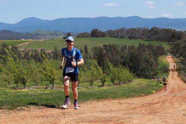 Runner in blue gear on a dirt trail with hills and trees in the background