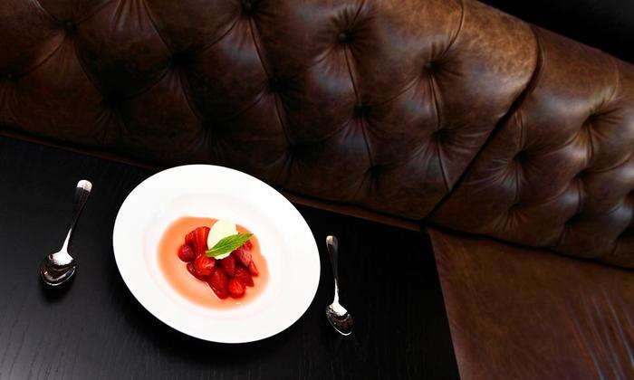 White plate with red dessert and mint on a dark table beside a tufted brown leather sofa