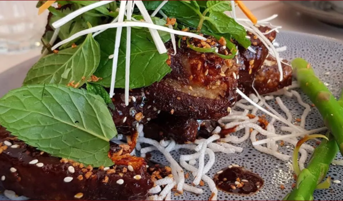 Gourmet meat dish with herbs, white sprouts, and green vegetables on a decorative plate