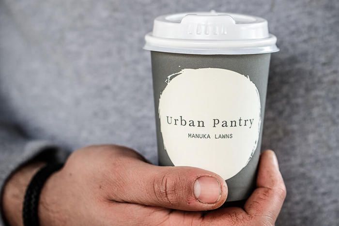 Hand holding a white Urban Pantry takeaway coffee cup with lid