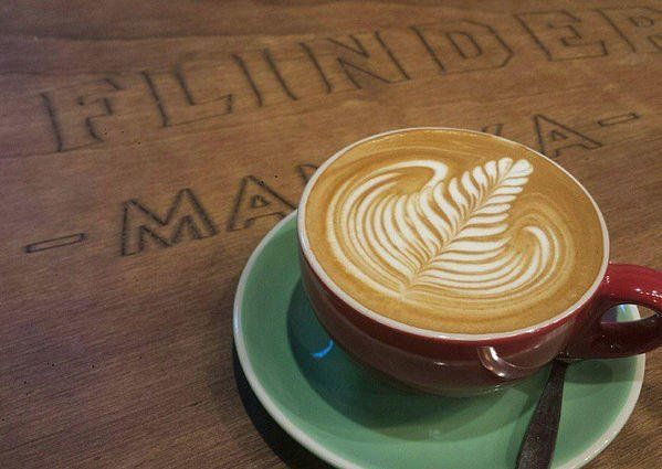 Latte with leaf latte art in a red cup on a green saucer atop a wooden table